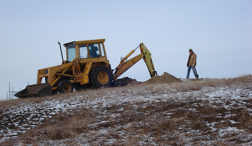 A backhoe digging planting holes on the frosty hillside